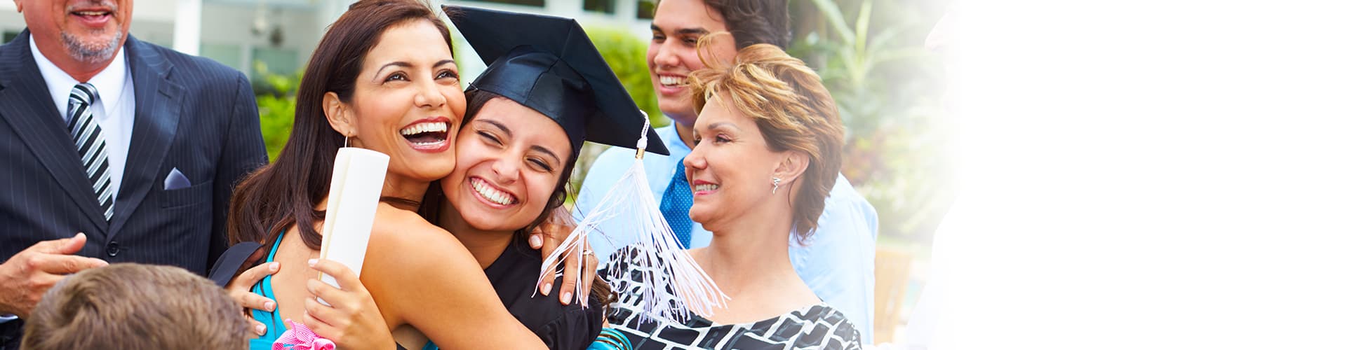 Woman hugging daughter who is wearing a cap and gown and holding her diploma