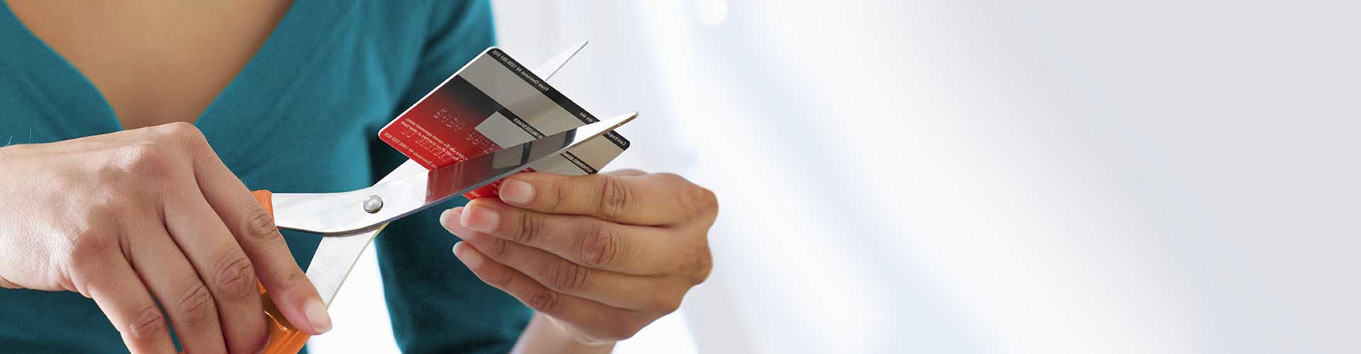 Someone cutting up red credit card with orange scissors