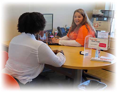 Ascentra team member sitting behind desk in orange shirt helping a member