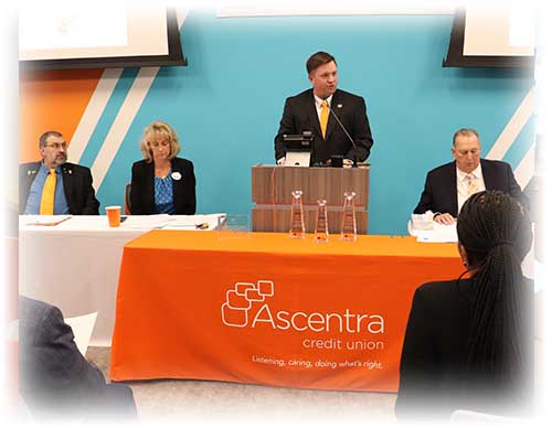Group of Ascentra board members standing up in front of blue, orange and white striped wall.