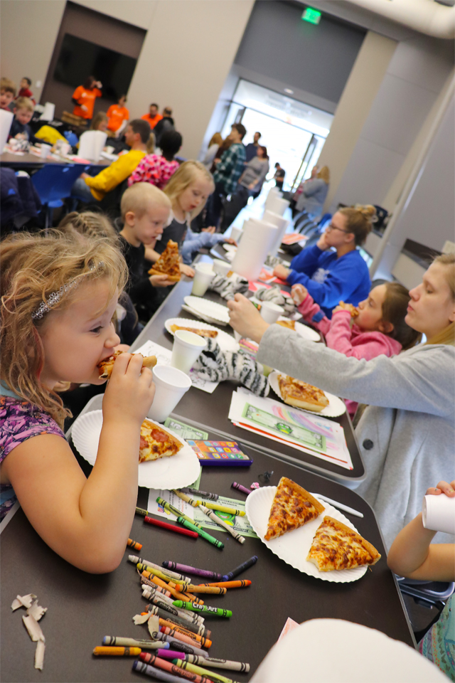 Kids coloring and eating pizza at a long table.