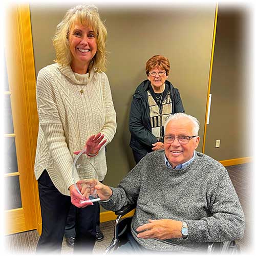 Linda Andry handing glass award to Larry Ketelsen with Larry's another board of director smiling in the background