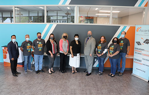Phyllis Thede and staff of Ascentra stand in front of orange, blue, and gray wall