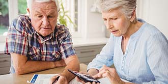 Two elderly people looking at financial documents and holding calculator ES