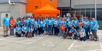 Group of Ascentra staff standing in front of orange building wearing blue shirts