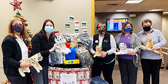 Ascentra Clinton South 14th branch standing in front of a holiday network toy box overflowing with toys. All the ladies are holding stuffed tigers that were donated.