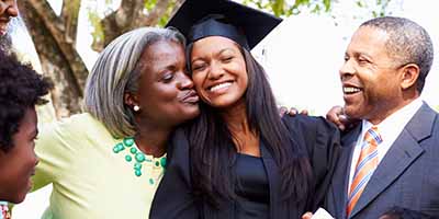 family hugging daughter who is wearing a graduation cap and gown and holding her diploma