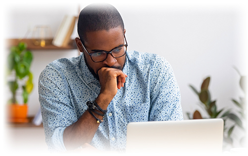 Man in blue shirt looking at his laptop with his hand to his mouth.