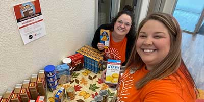 Two women taking a selfie with food donations displayed on a table